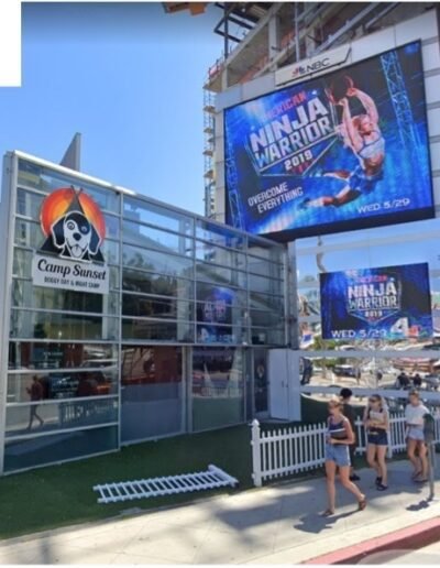 A group of people walk past a large billboard in front of a building.